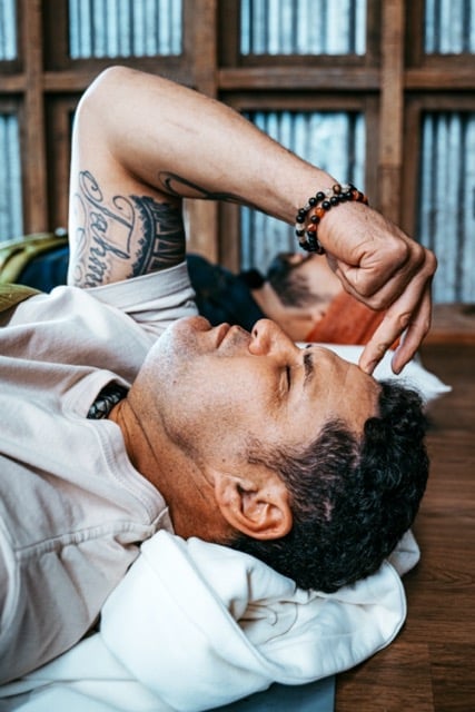A man laying on the floor practising breathwork with a finger on his forehead.